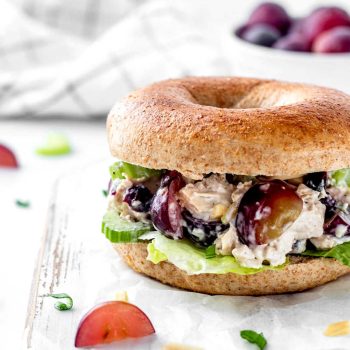 Chicken salad with grapes and almonds loaded onto a bagel with lettuce.