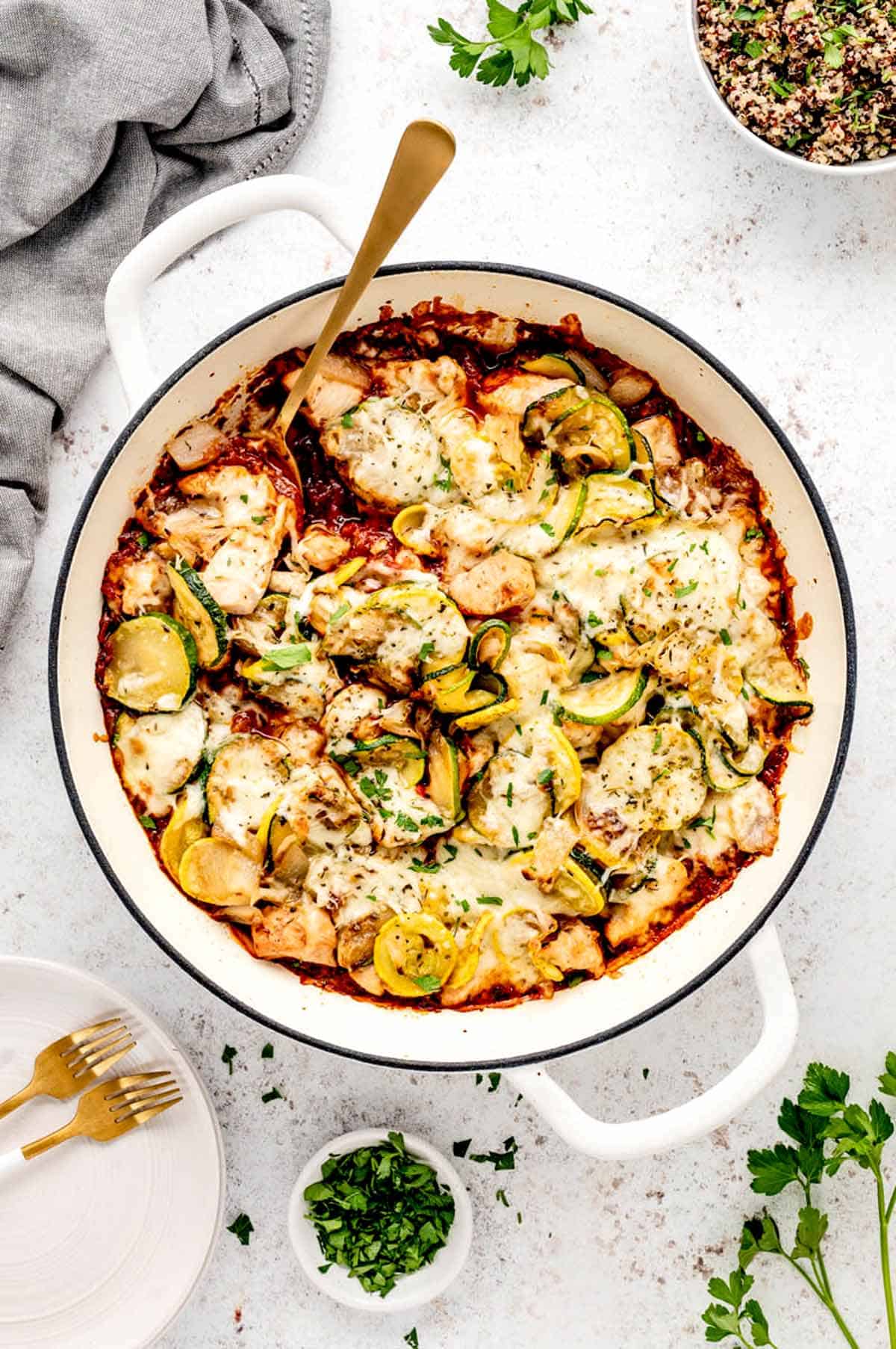 The baked chicken zucchini casserole in a white Dutch oven with a spoon in it.