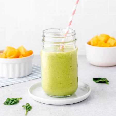 A green yogurt and banana free smoothie in a jar on a small plate.