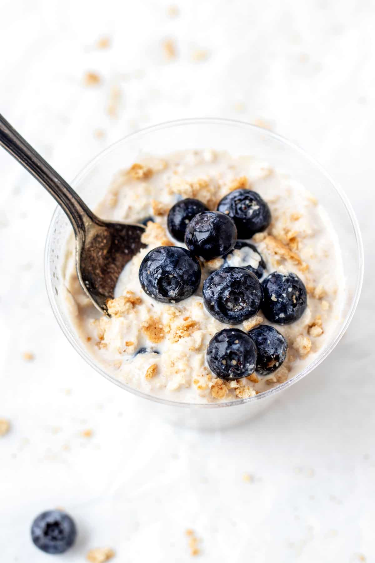 A spoon digging into creamy cheesecake overnight oats topped with fresh blueberries.