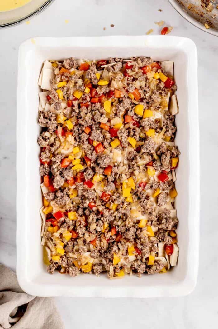 A second layer of cooked ground sausage and veggies spread evenly over the tortilla layer in a baking dish.