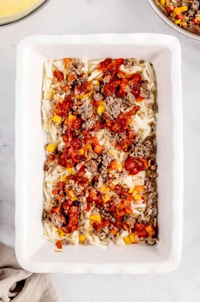 A layer of salsa on top of the sausage, vegetables and hash browns in a baking dish.