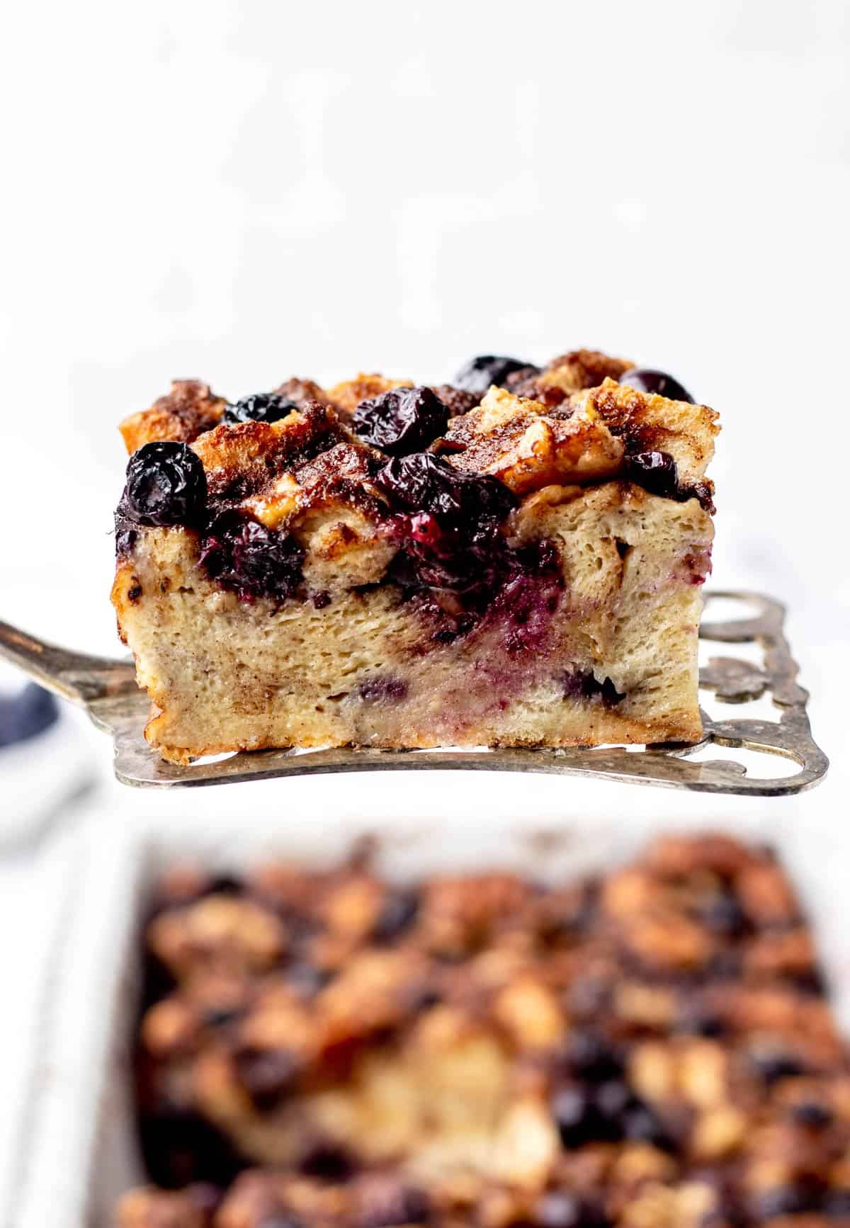 A slice of blueberry French toast casserole being held up on a serving spatula.