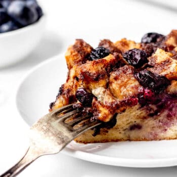Close up image of a fork digging into a piece of blueberry French toast casserole.