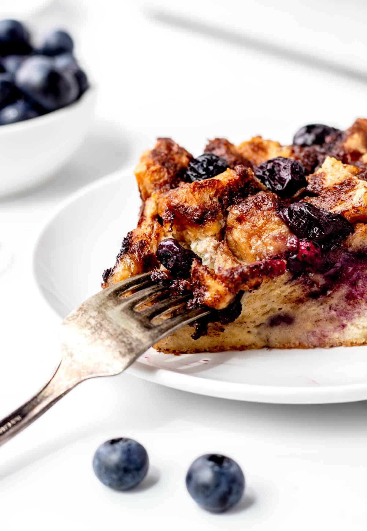 A fork digging into a slice of French toast casserole with blueberries.