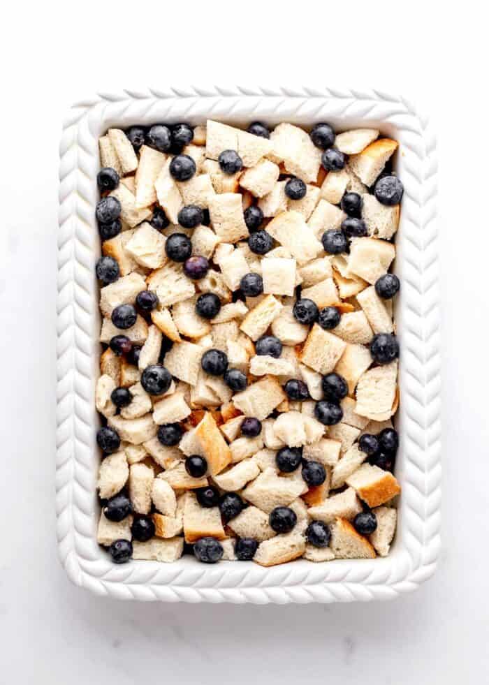 Sourdough bread and blueberries layered in a white casserole dish.