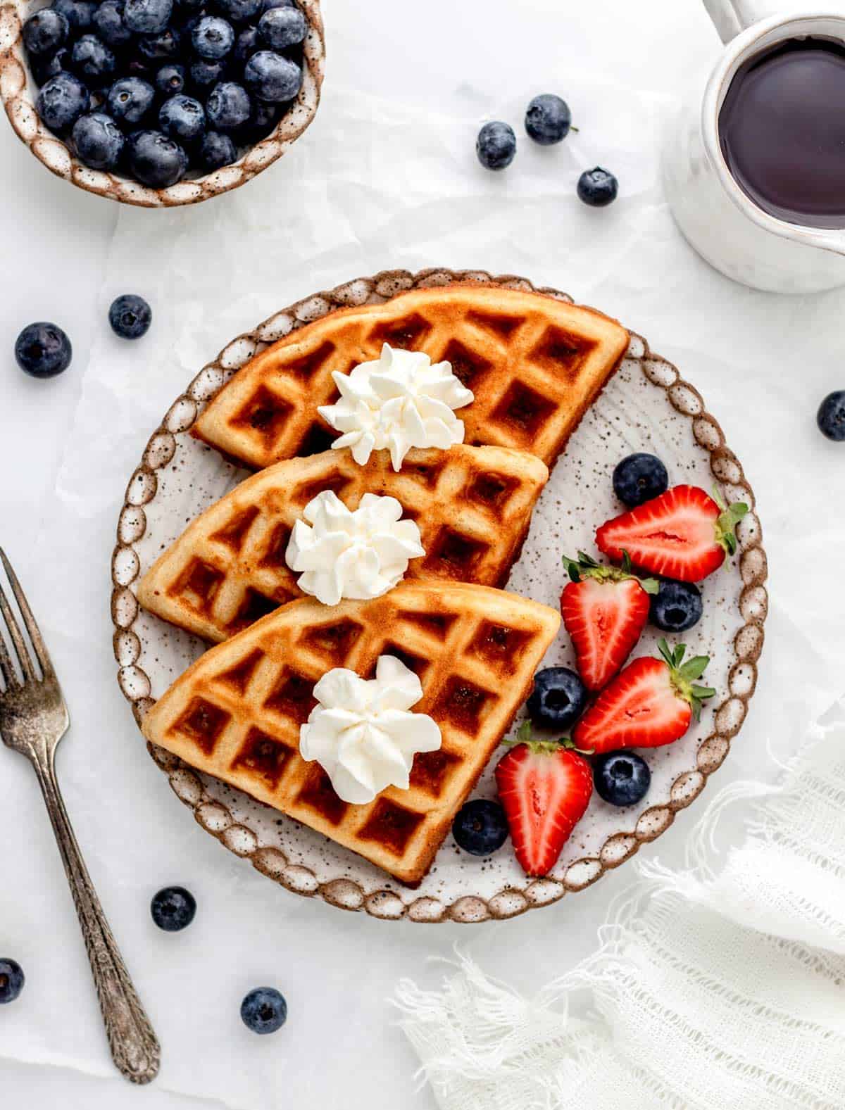 An overhead image of almond flour waffles on a plate with whipepd cream and fresh berries.
