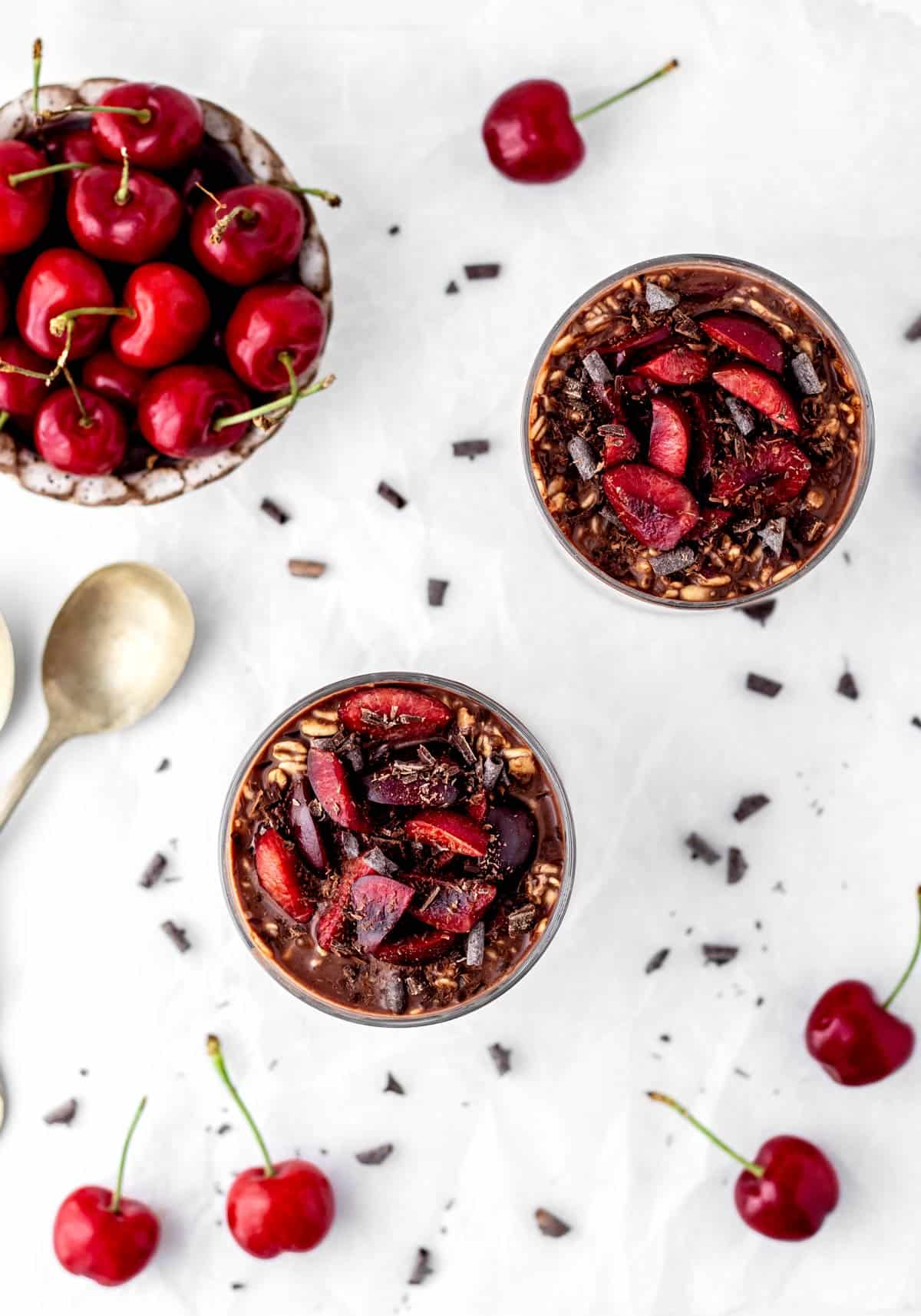 Two glasses with chocolate cherry overnight oats with fresh cherries and chocolate on top.