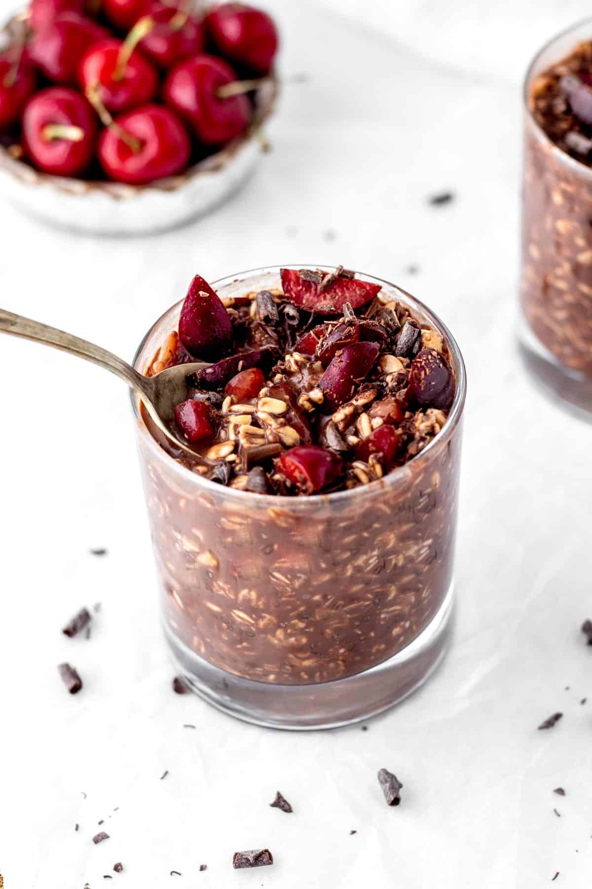 A spoon digging into a glass of chocolate cherry overnight oats.