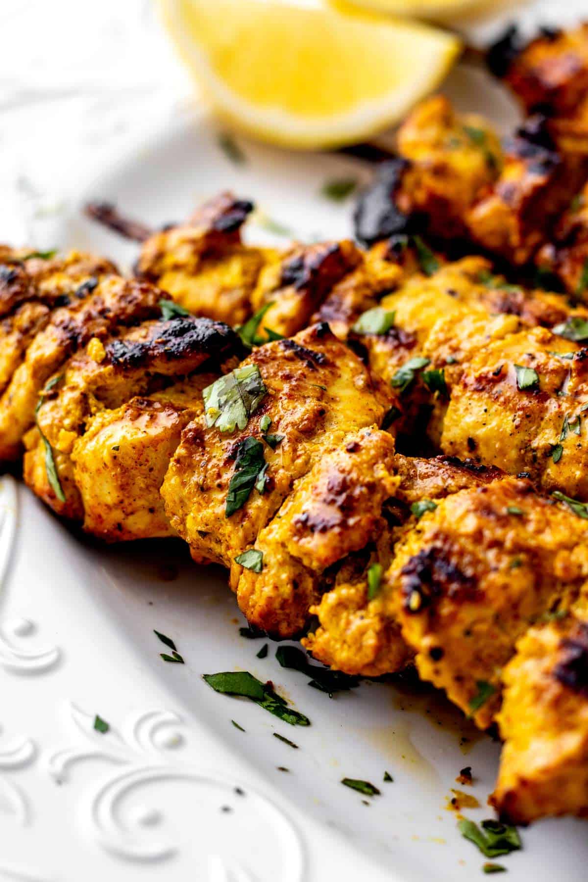 Close up image of chicken tikka kebabs on plate topped with cilantro.