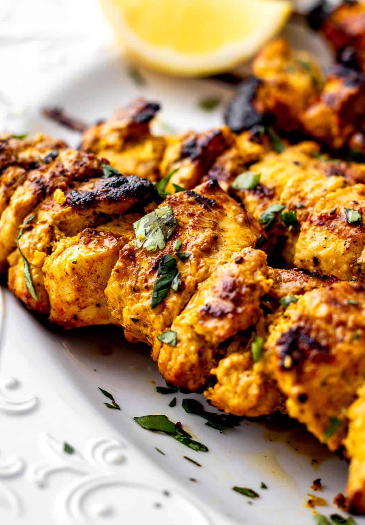 Close up of chicken tikka skewers on a white tray.