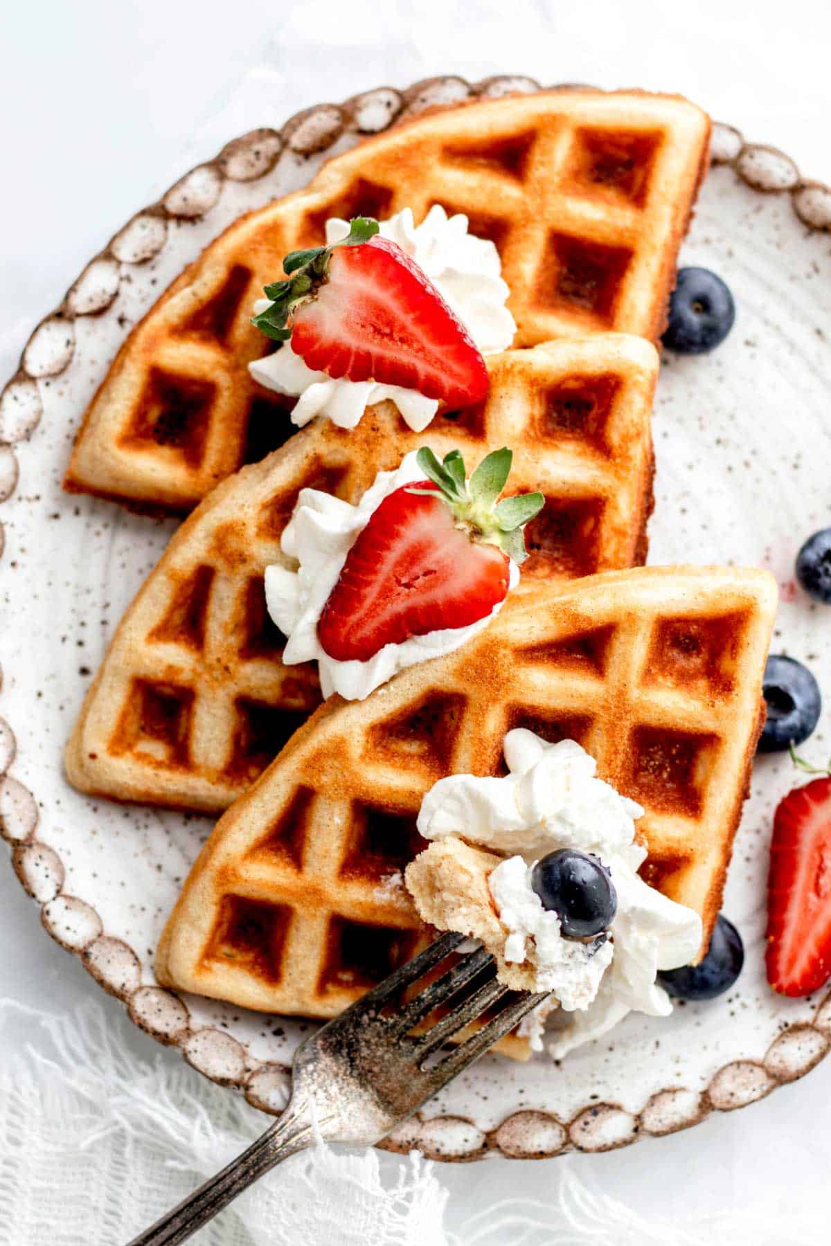 A overhead image of a fork poking a piece of low carb waffles with whipped cream and berries.