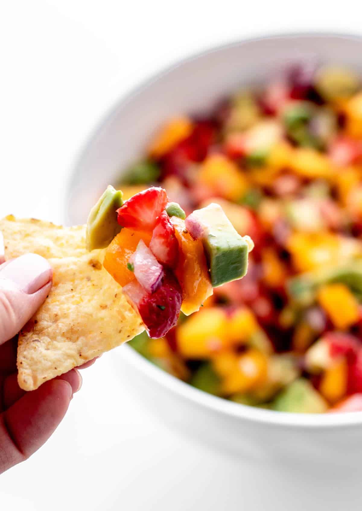 A tortilla chip scooping up some strawberry mango salsa.