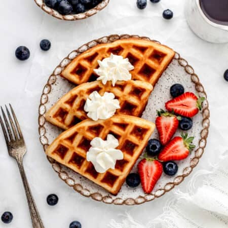Paleo waffles on a plate topped with whipped cream next to fresh berries.