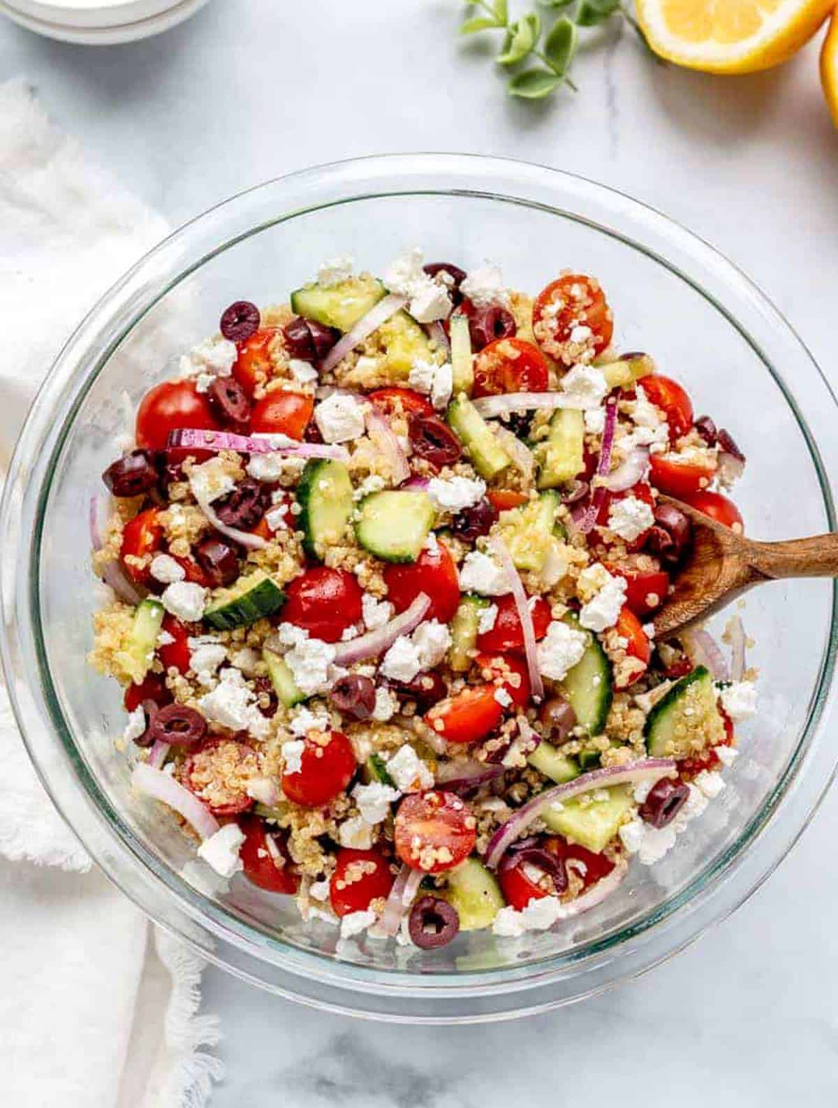 Greek quinoa salad in a large bowl with a wooden spoon digging in.