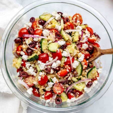 A large bowl of Greek quinoa salad with a wooden spoon.