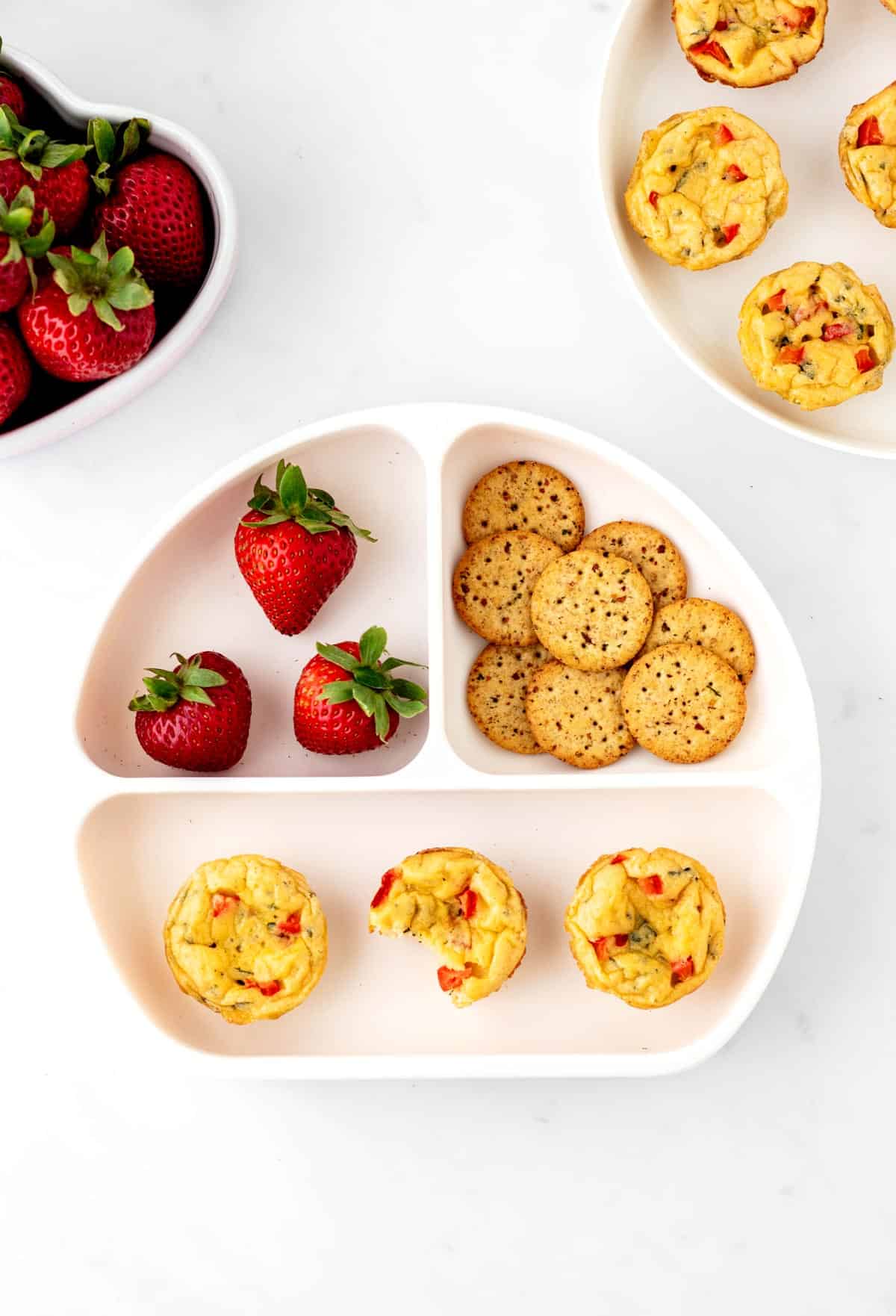 Mini egg bites on a plate with crackers and strawberries.