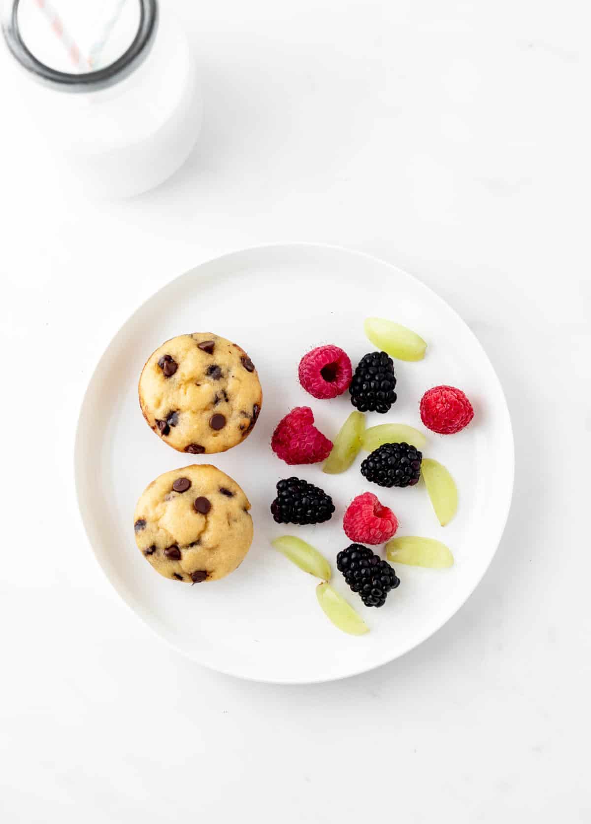Mini chocolate chip muffins on a plate with fresh fruit.