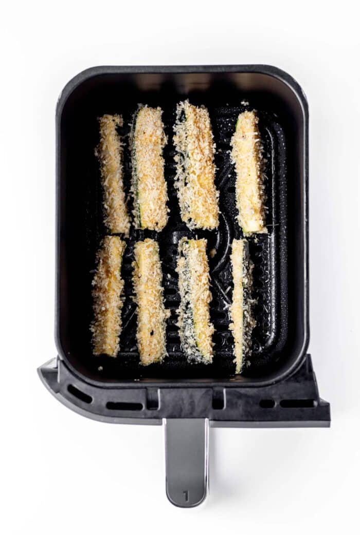 Parmesan zucchini fries in an air fryer basket ready to be cooked.