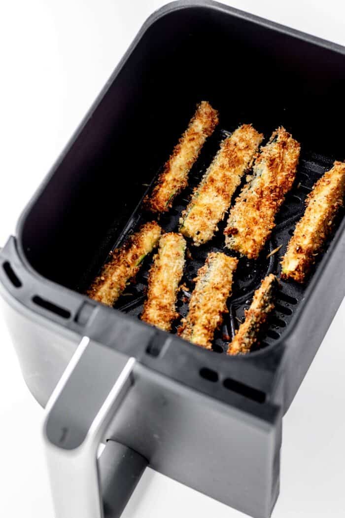 Cooked zucchini fries in air fryer basket.