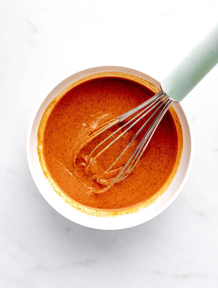 Spicy Thai peanut sauce being whisked together in a bowl.