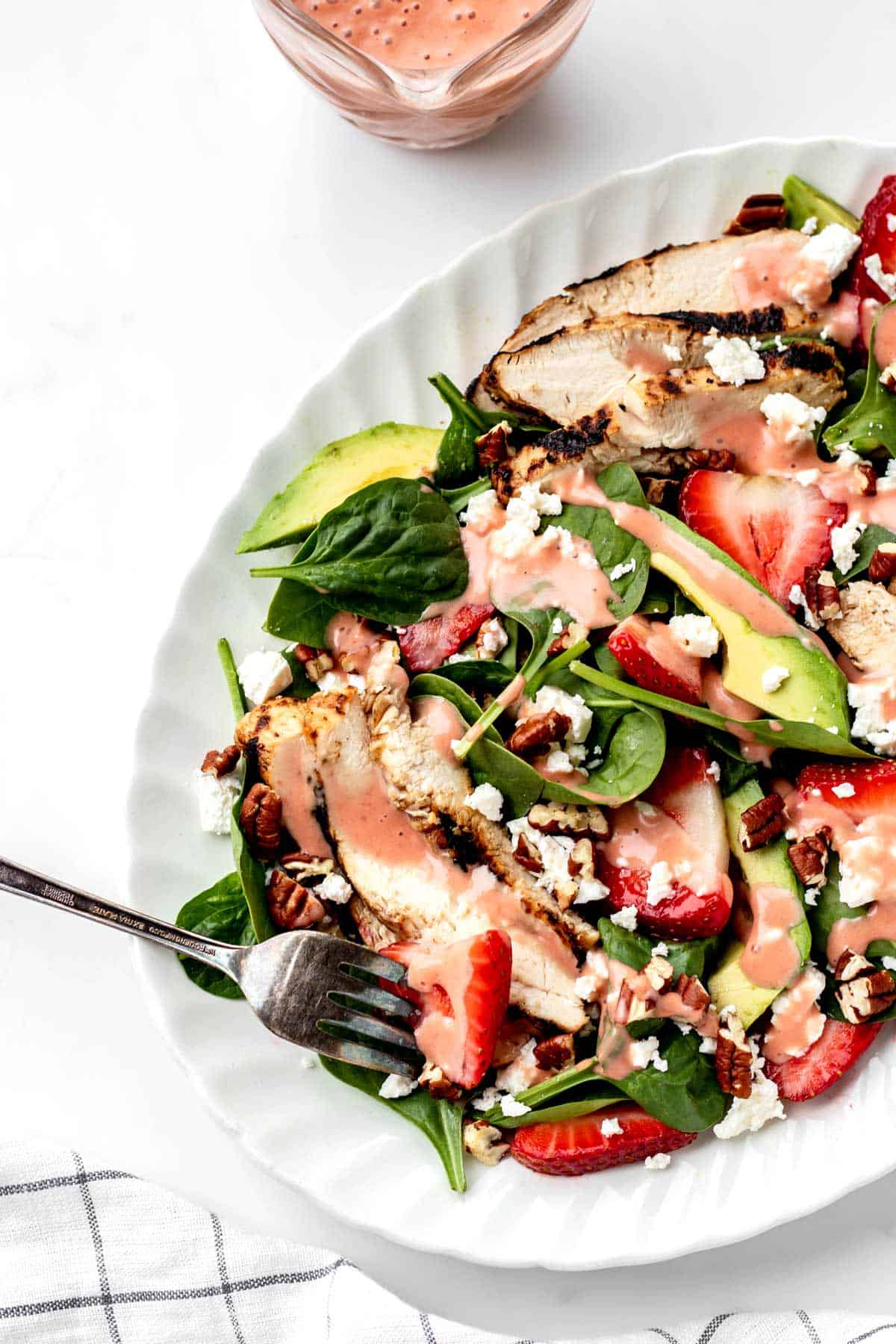 A fork poking some strawberry chicken salad drizzled in strawberry balsamic vinaigrette.