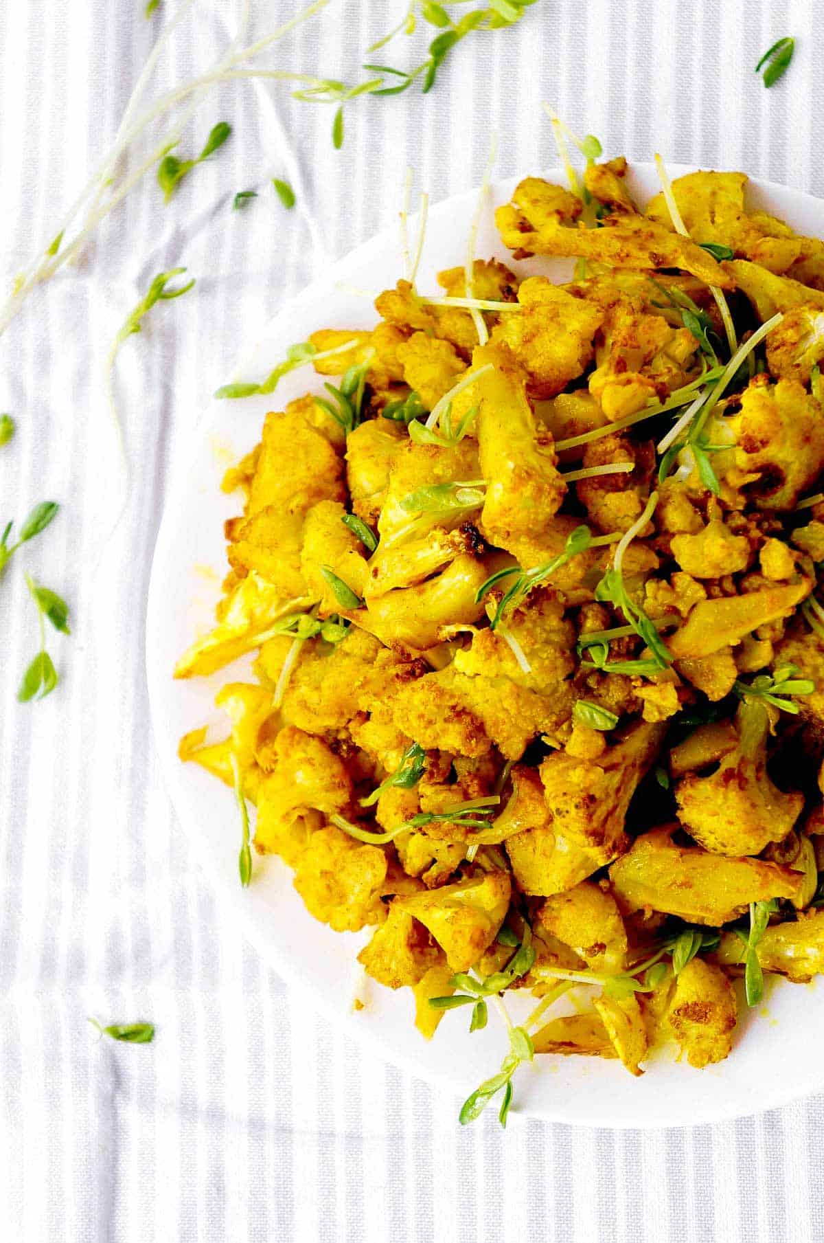 A plate of turmeric cauliflower topped with micro greens.