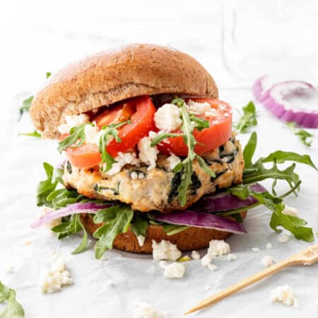 A chicken feta burger topped with tomatoes, arugula and red onion.
