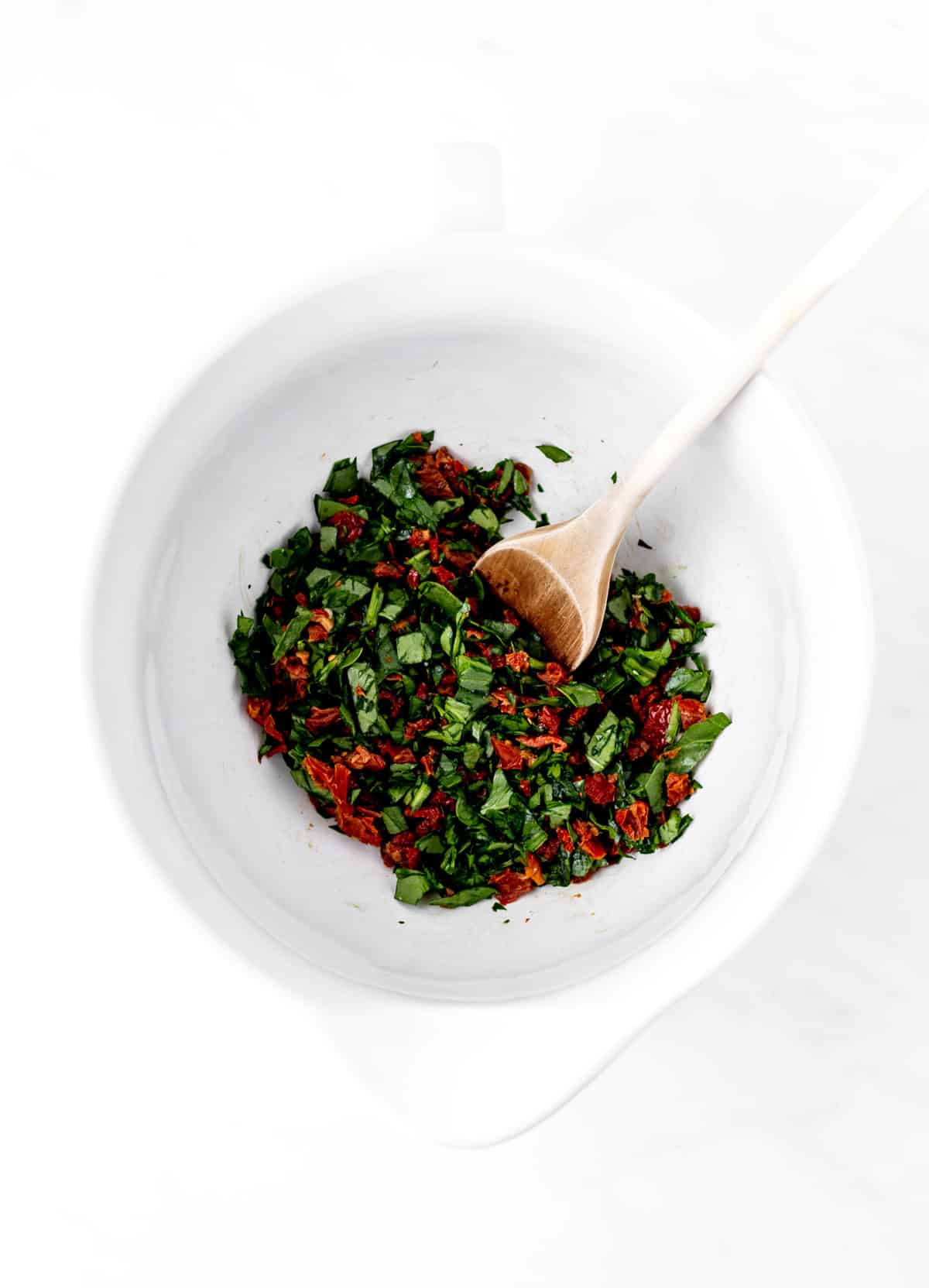 Spinach and sun-dried tomatoes being mixed together in a bowl.