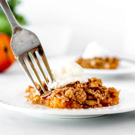 A fork digging into some healthy peach crisp with oats and whipped cream.