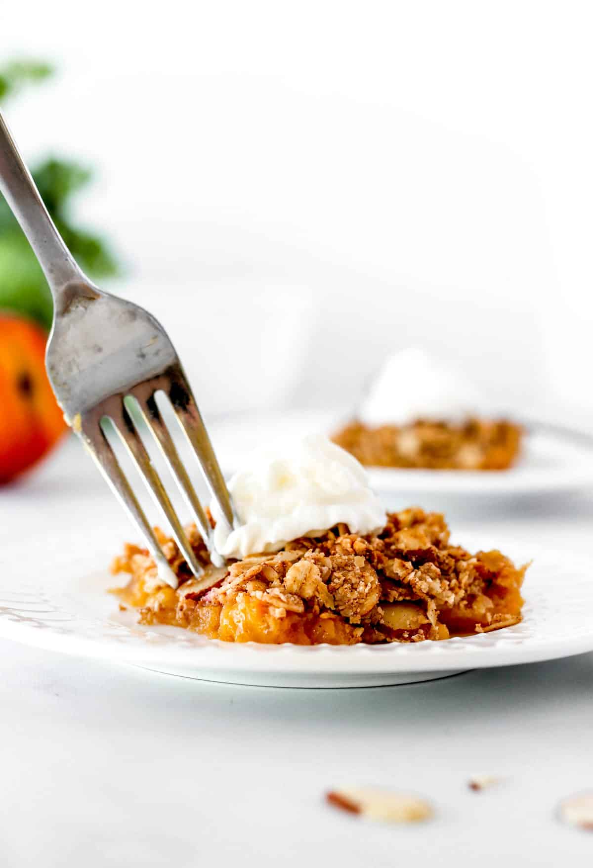 A fork digging into the healthy peach crisp on a plate.