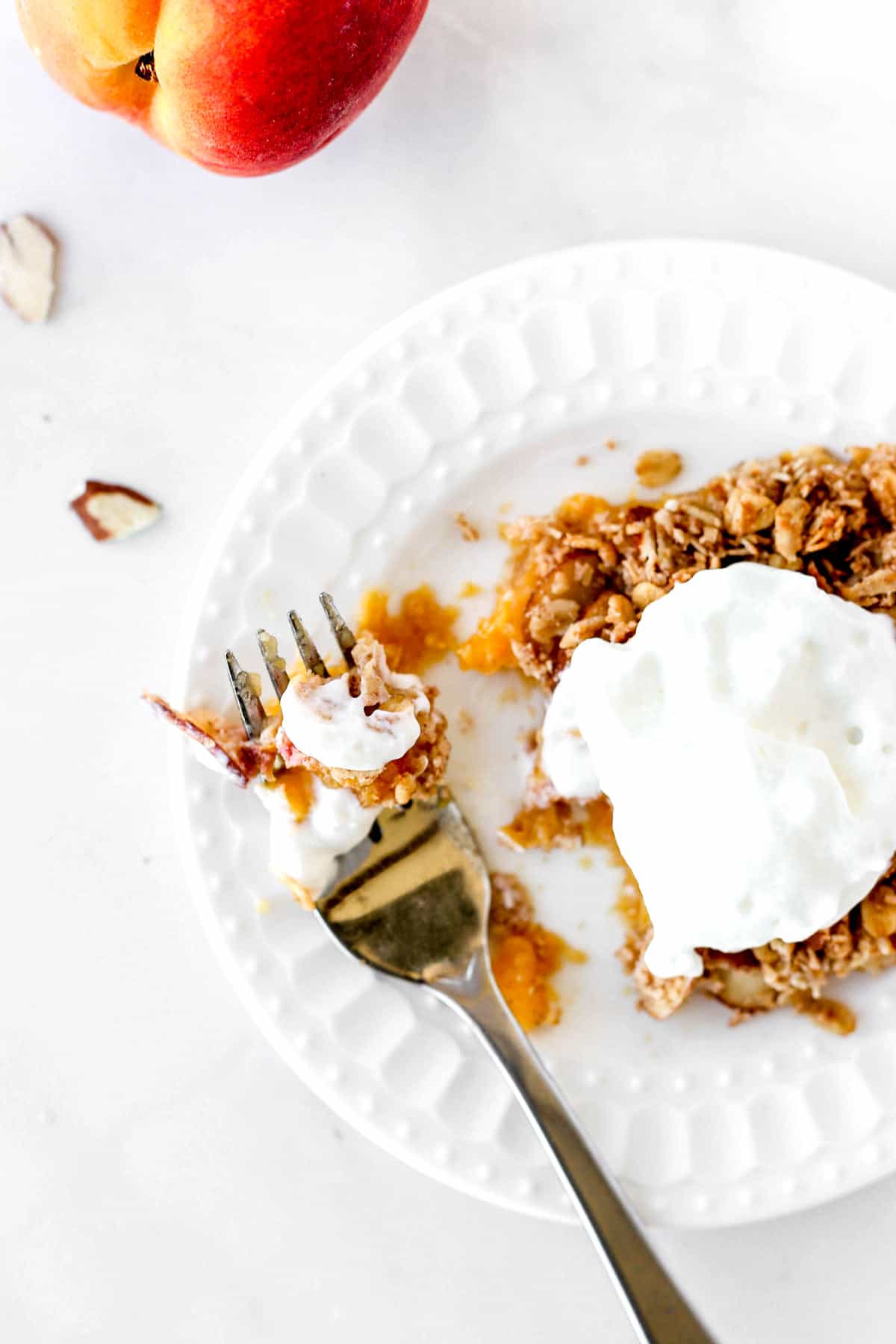 Overhead image of a fork with some peach crisp with oats and whipped cream.