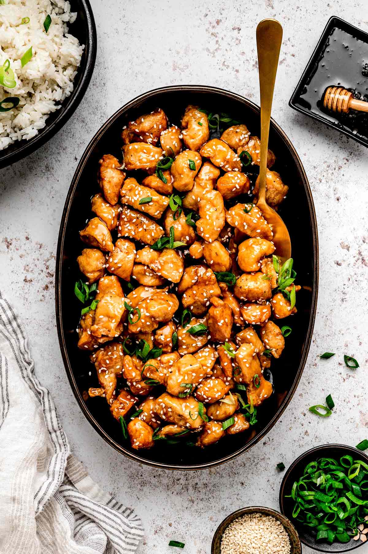 Crispy honey sesame chicken pieces in an oval serving dish with a spoon.