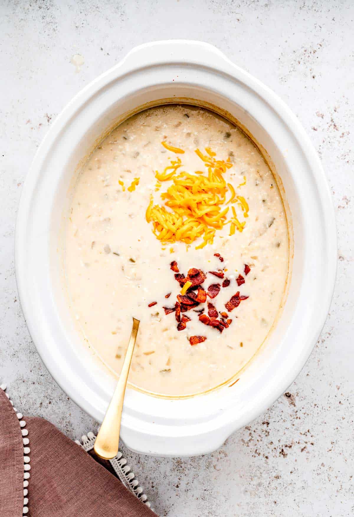 Creamy potato soup in a white crockpot with a sprinkle of bacon and cheese.