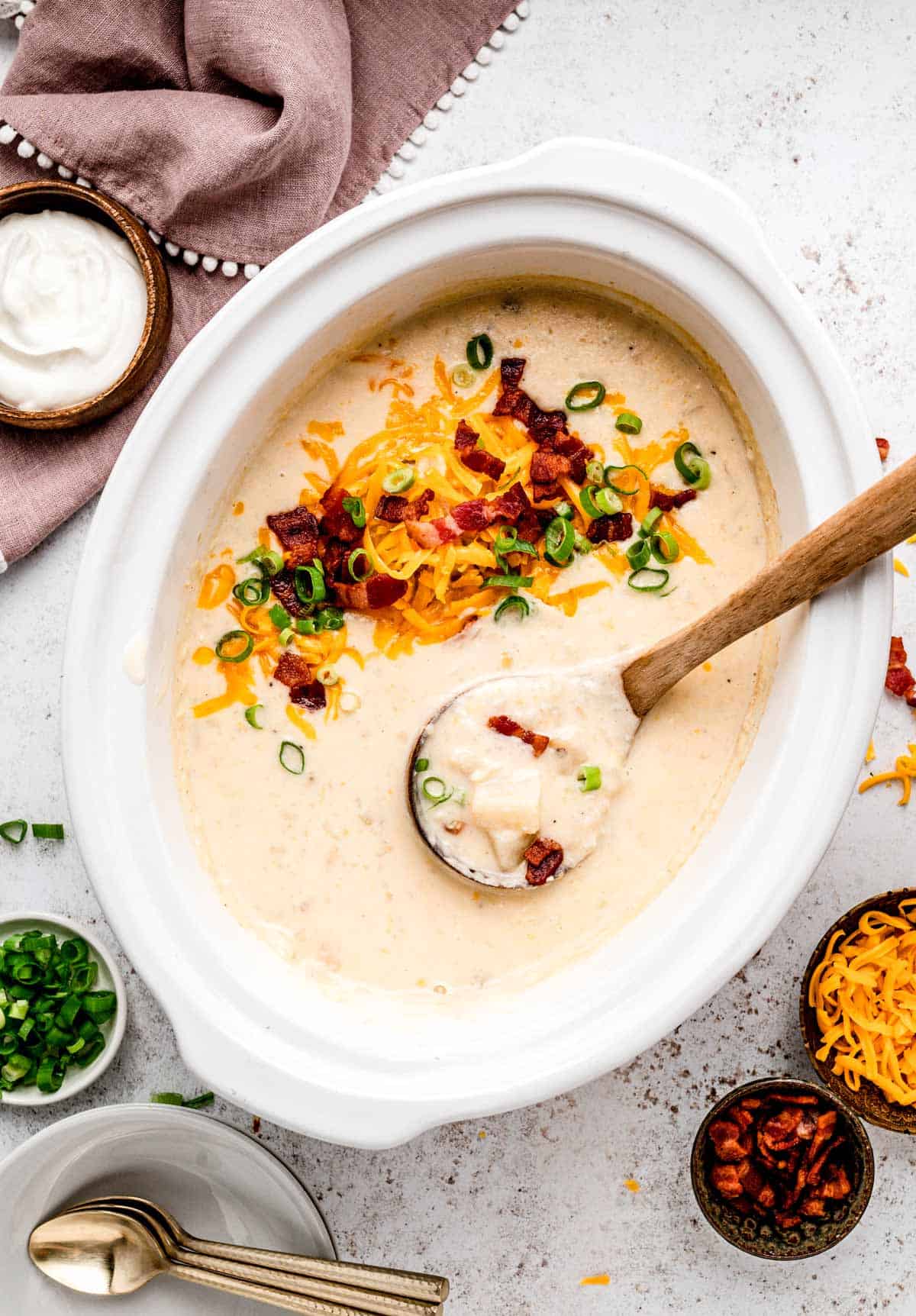 Slow cooker potato soup with cream cheese in a white crockpot with toppings.