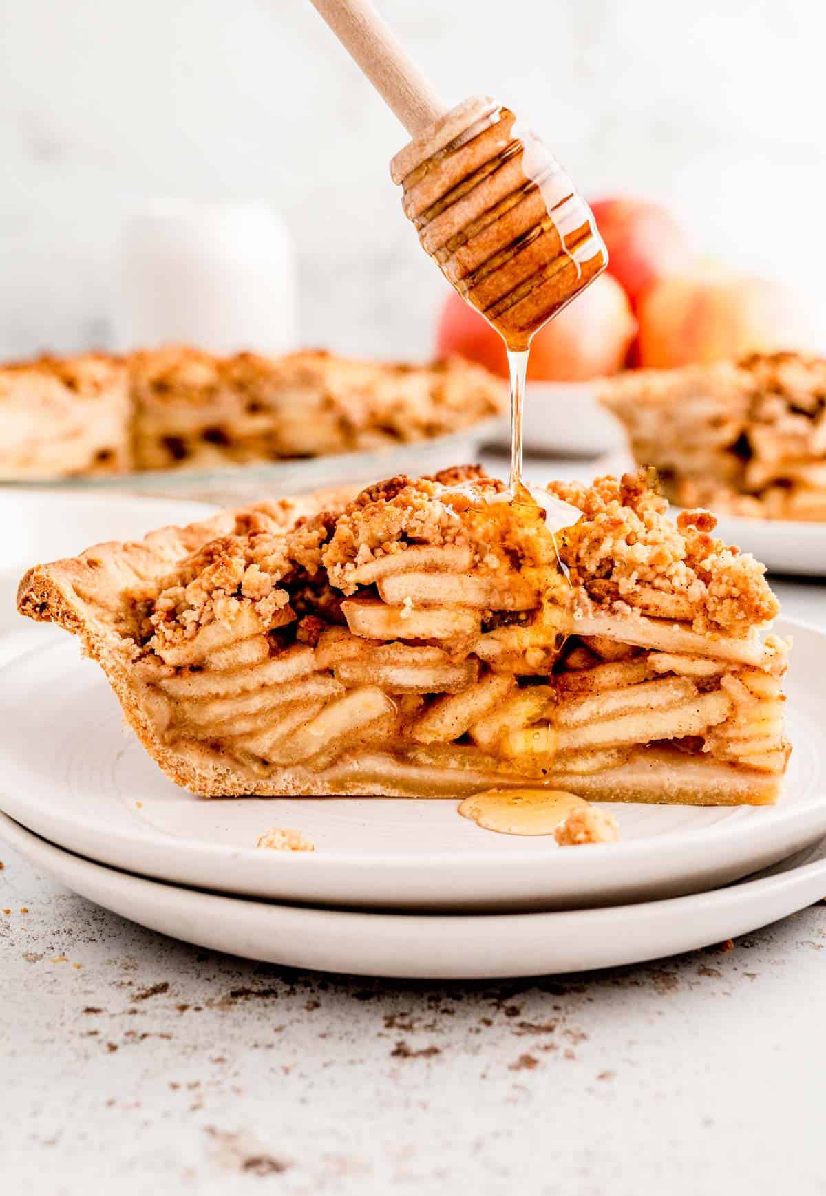 A honey dipper drizzling honey over a slice of healthy apple pie.