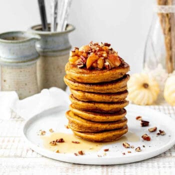 A stack of pumpkin protein pancakes with apple topping and chopped nuts.