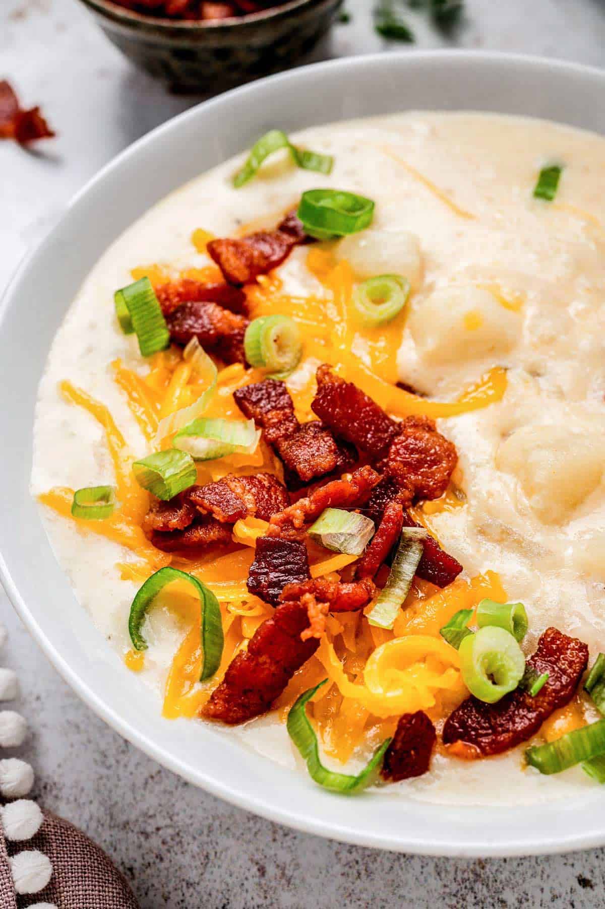 A close up image of slow cooker loaded baked potato soup in a white bowl.