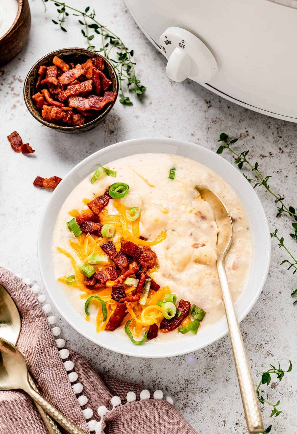 A spoon digging into a bowl of healthy slow cooker potato soup with toppings.