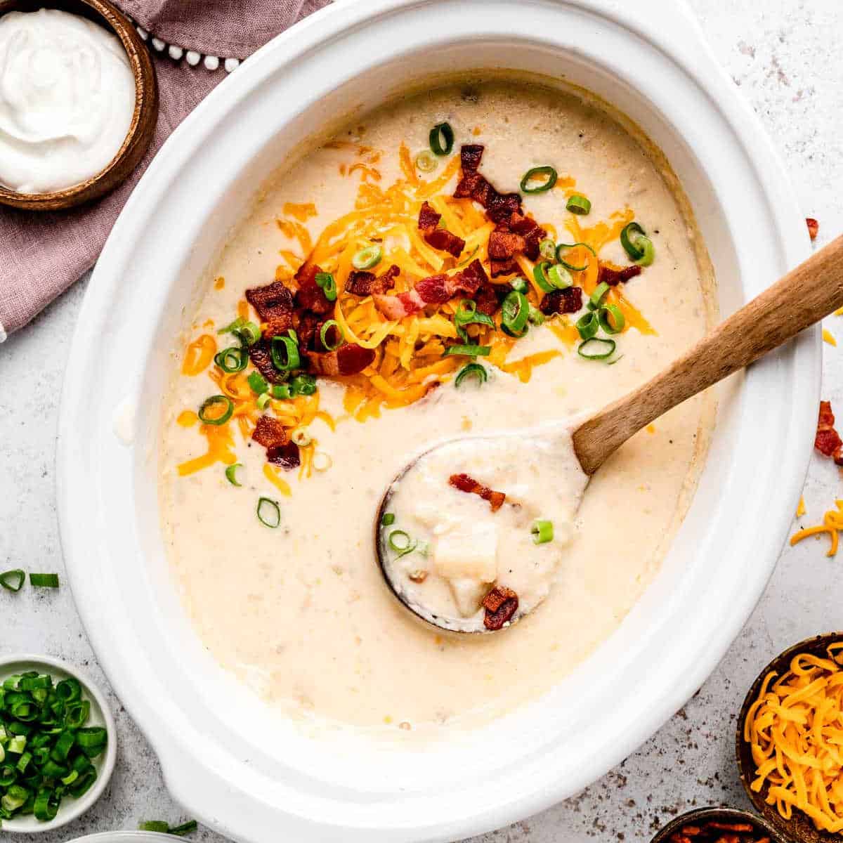 A wooden spoon scooping up some slow cooker loaded baked potato soup.