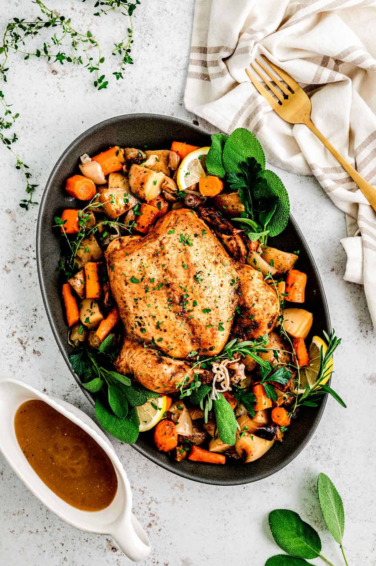 A whole chicken on a platter with potatoes, vegetables and fresh herbs.