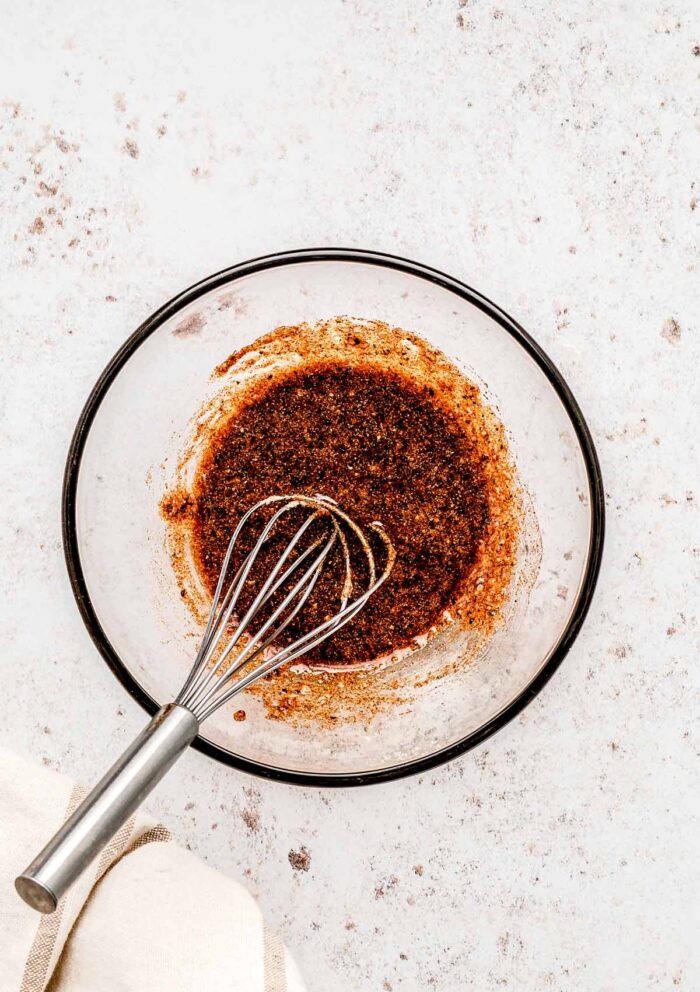 A whisk combining the spice mixture and olive oil in a bowl.