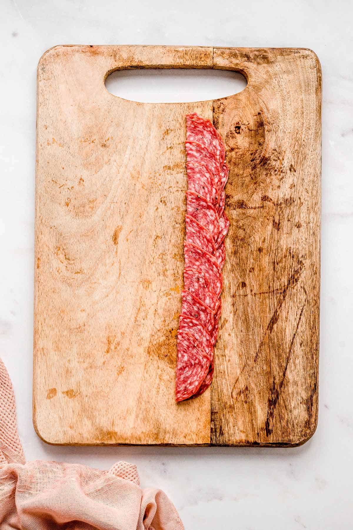 Salami slices cut in half on a wooden cutting board.