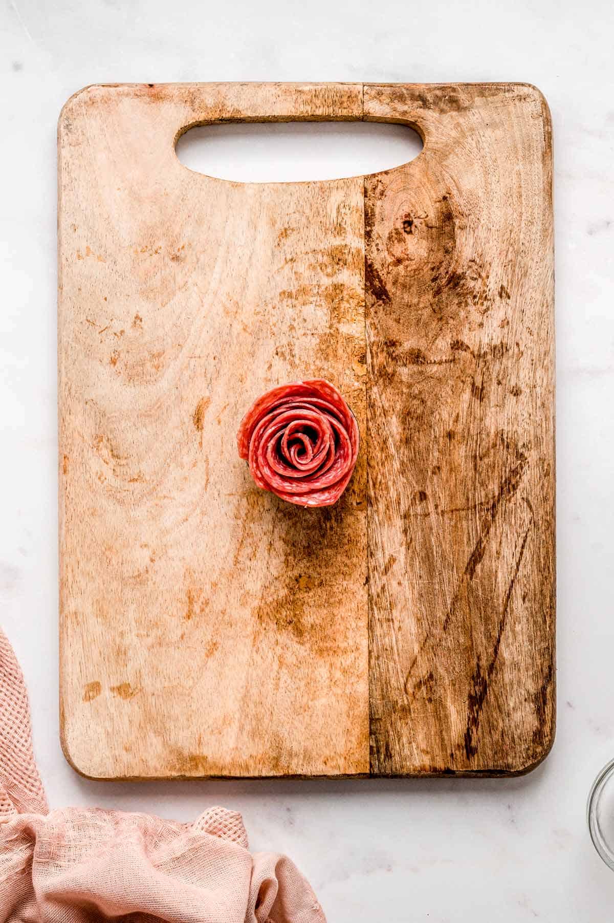 A salami rose on a wooden cutting board.