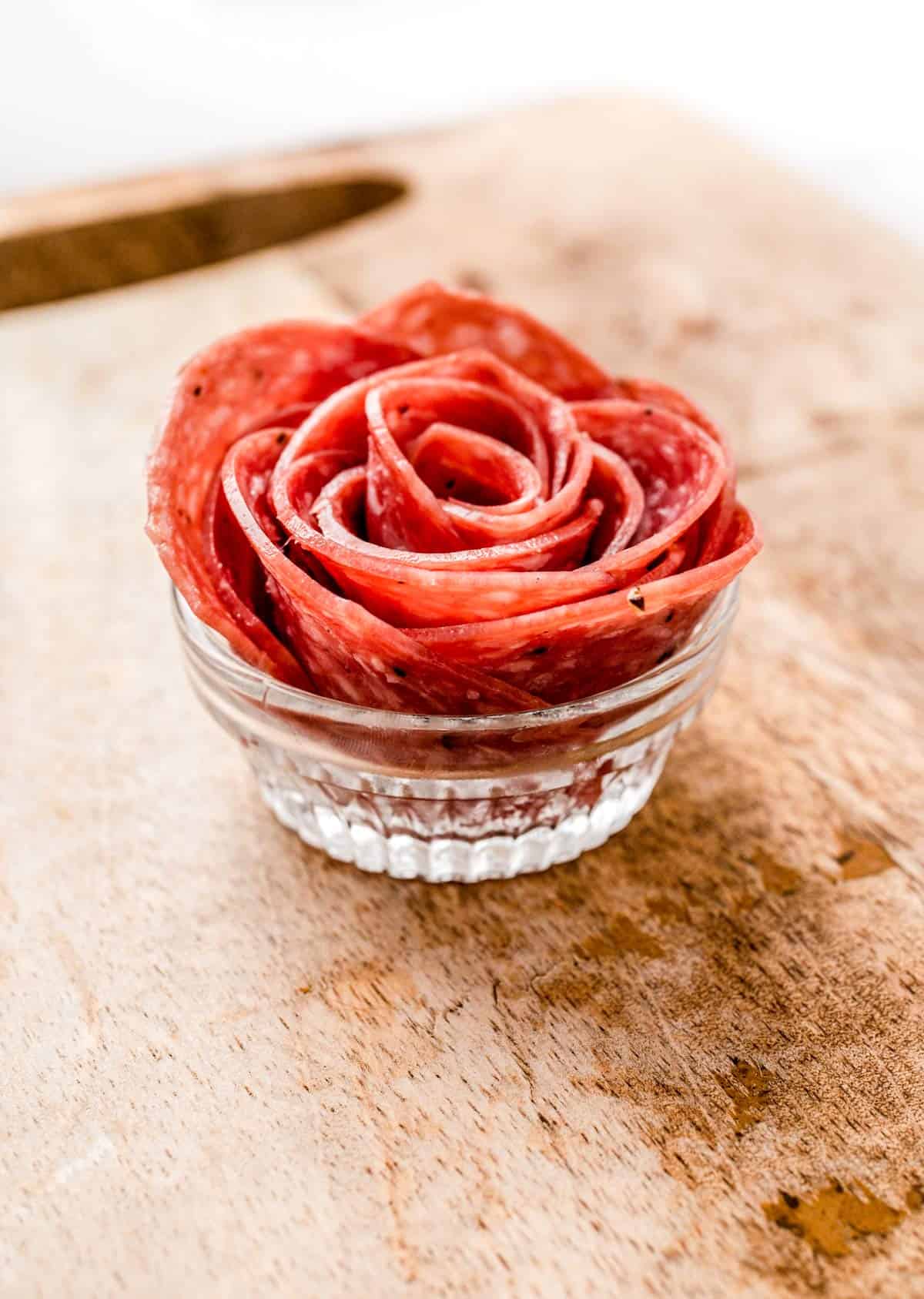 A salami rose on a wooden cutting board.
