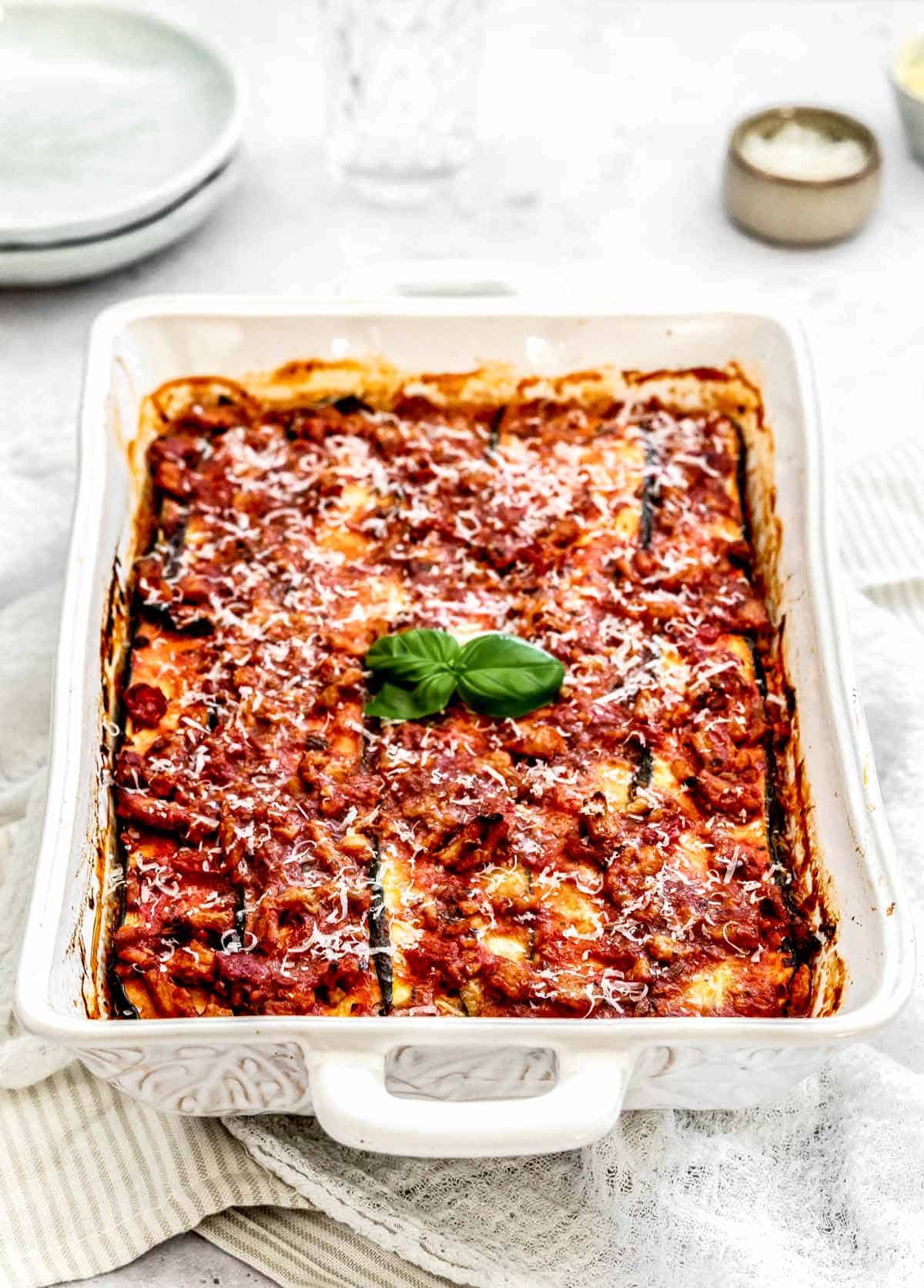 Zucchini lasagna with ground turkey in a white baking dish topped with basil.