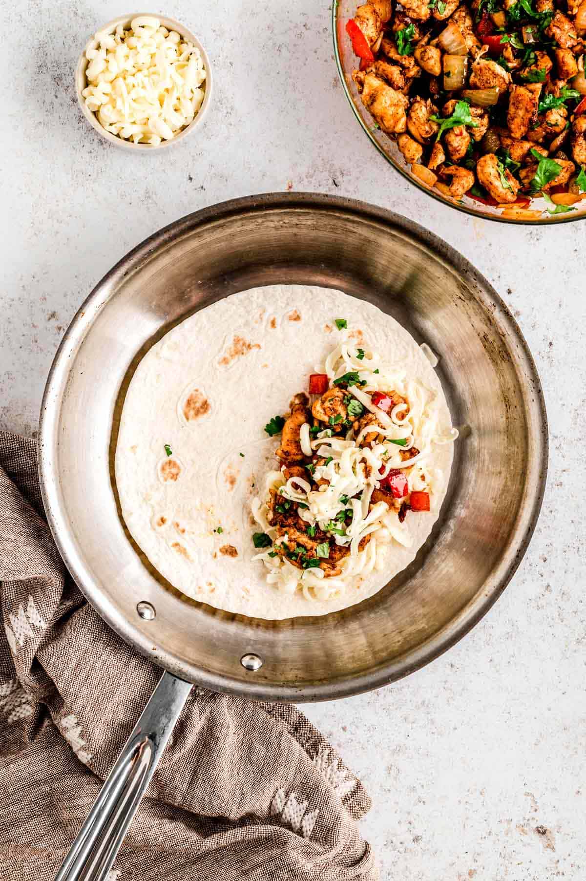 Chicken mixture on one half of a tortilla in a frying pan.