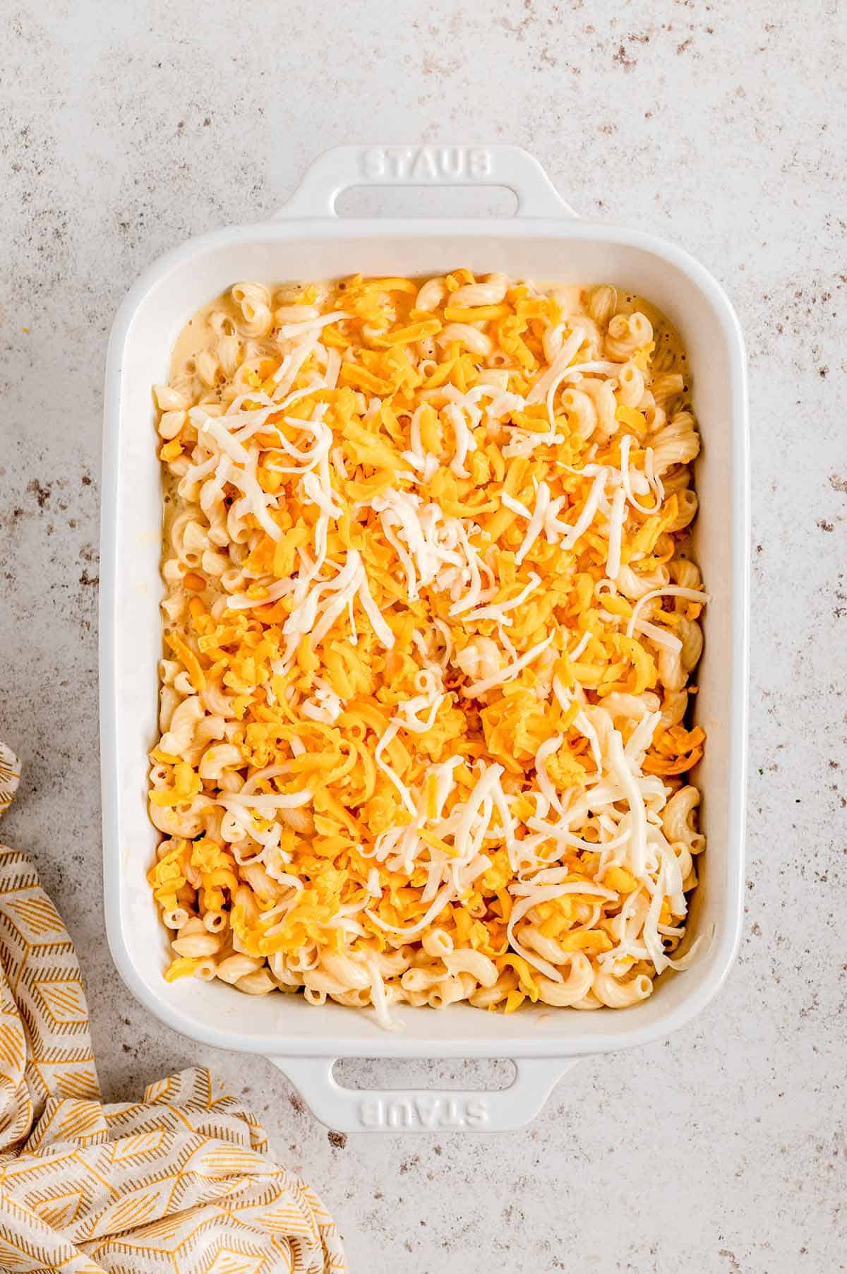 Mac and cheese without flour in a casserole dish with shredded cheese on top.