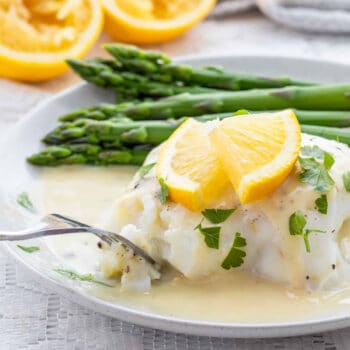 White fish with lemon garlic sauce drizzled over top with some lemon slices.