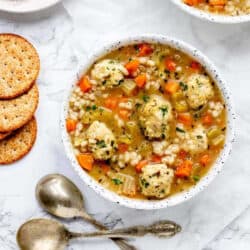 A bowl of mini chicken meatball soup with crackers.
